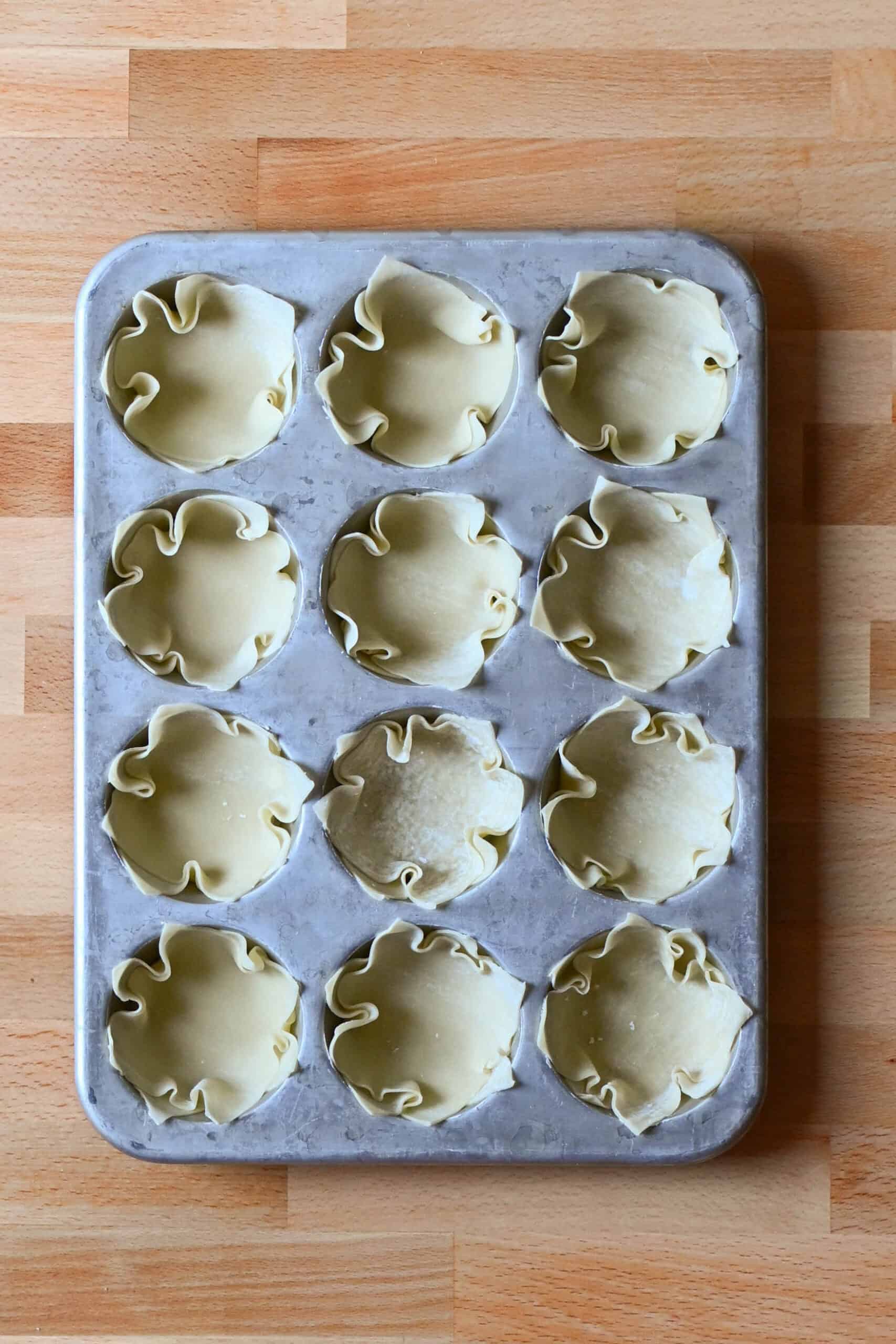 Wonton wrappers pressed into a 12-cup muffin tin.
